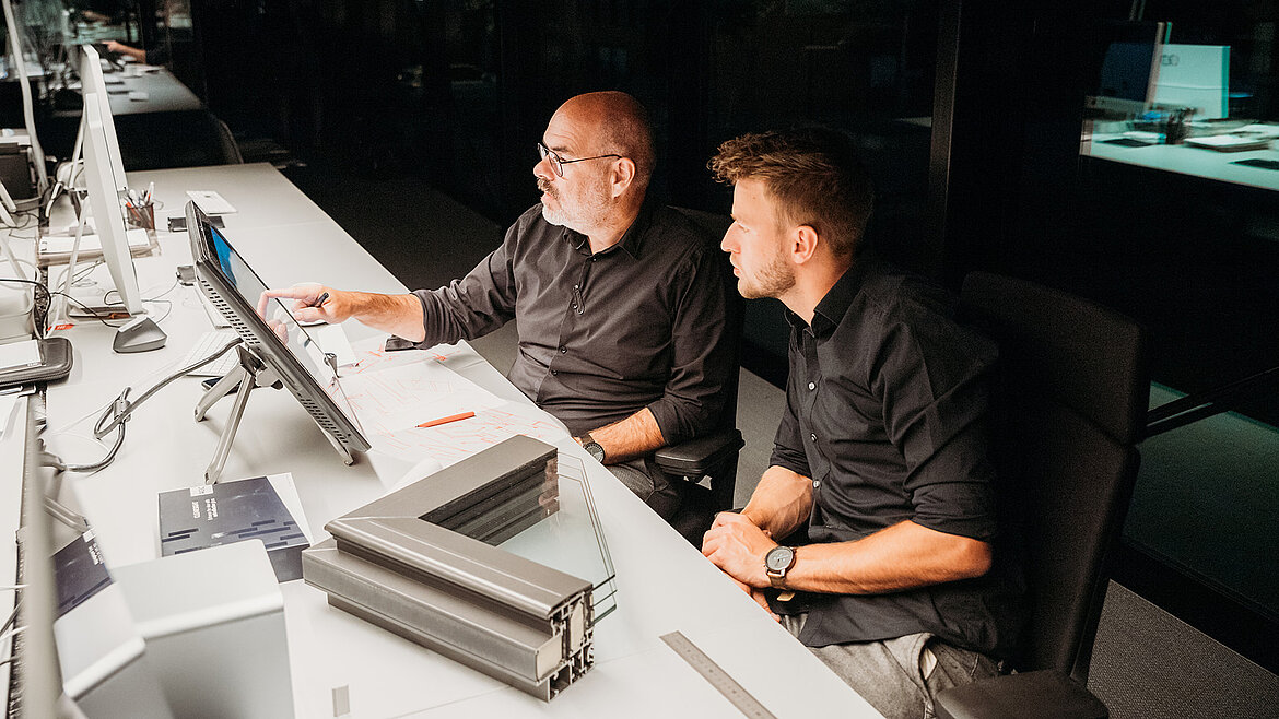 Zwei Männer in schwarzer Kleidung arbeiten gemeinsam an einem Computerarbeitsplatz.