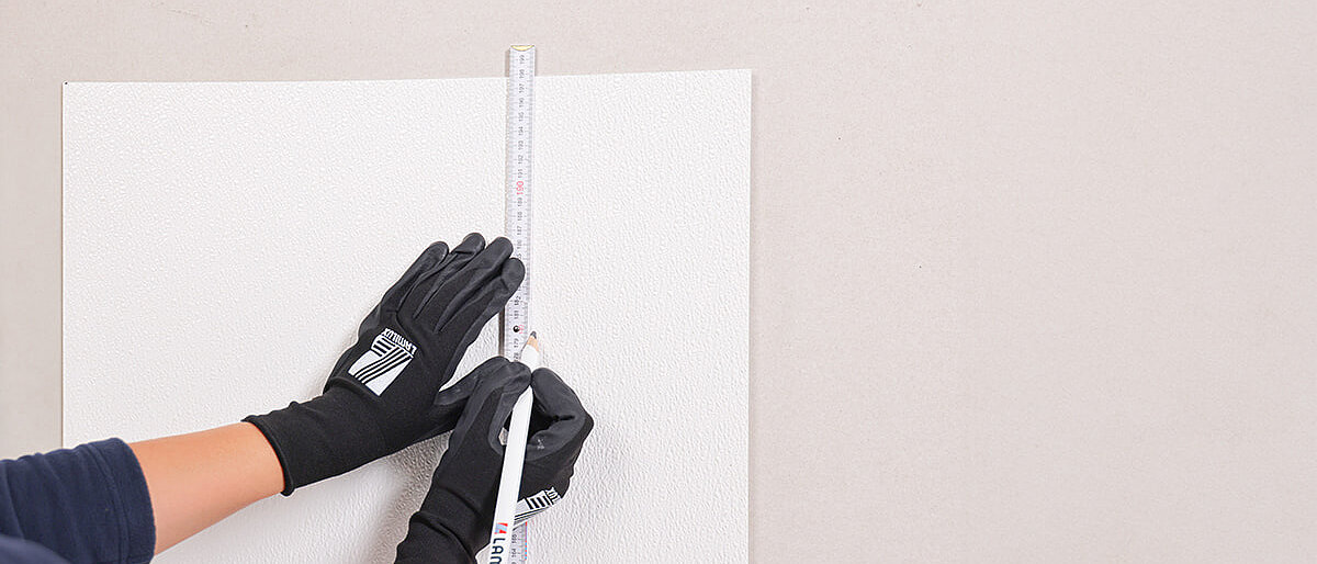 Person mit Handschuhen markiert mit einem Lineal und Bleistift auf einer weißen Oberfläche
