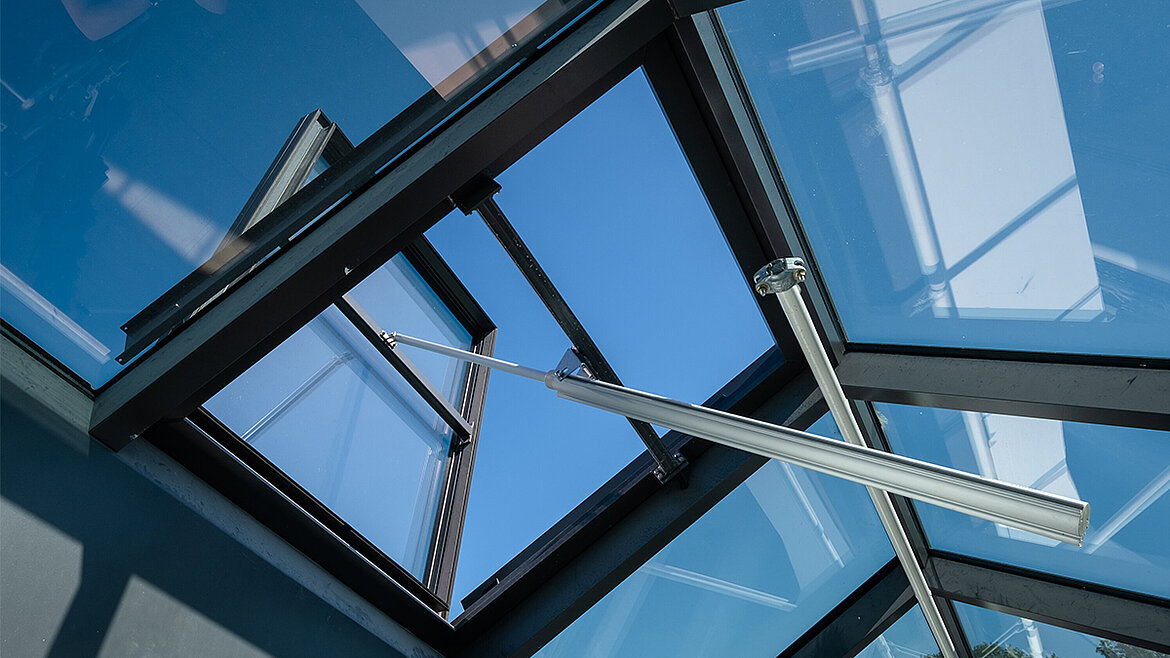 Geöffnetes Dachfenster mit Aluminiumrahmen und silbernen Stützstreben vor blauem Himmel