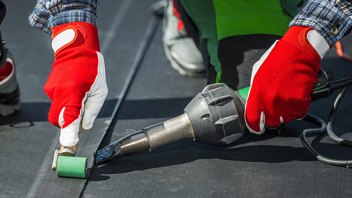 Detailaufnahme eines Handwerkers beim Verschweißen einer Dachabdichtungsbahn mit Heißluftföhn