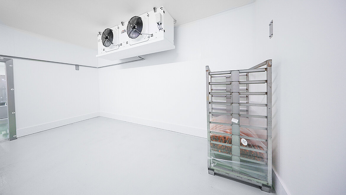 Leerer Kühlraum mit einem Metallregalwagen und Deckenventilatoren.
