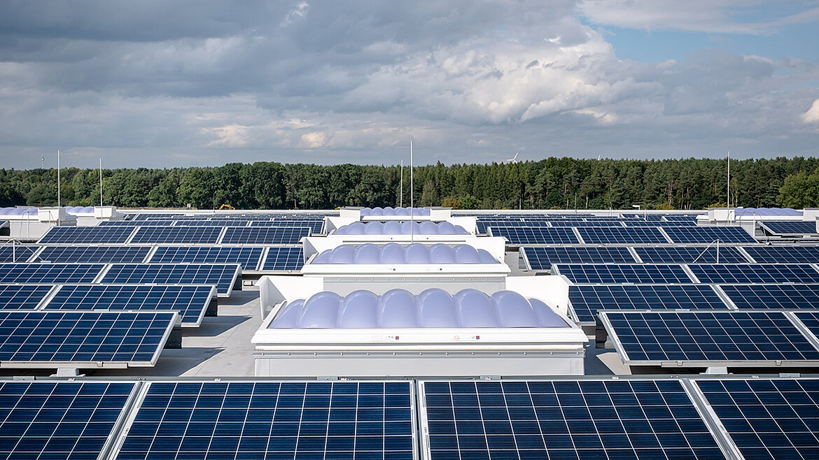 Flachdach mit zahlreichen Solarmodulen und integrierten Lichtkuppeln vor bewaldeter Landschaft