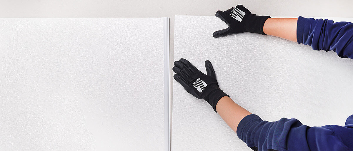 Person richtet zwei weiße Platten an der Wand aus