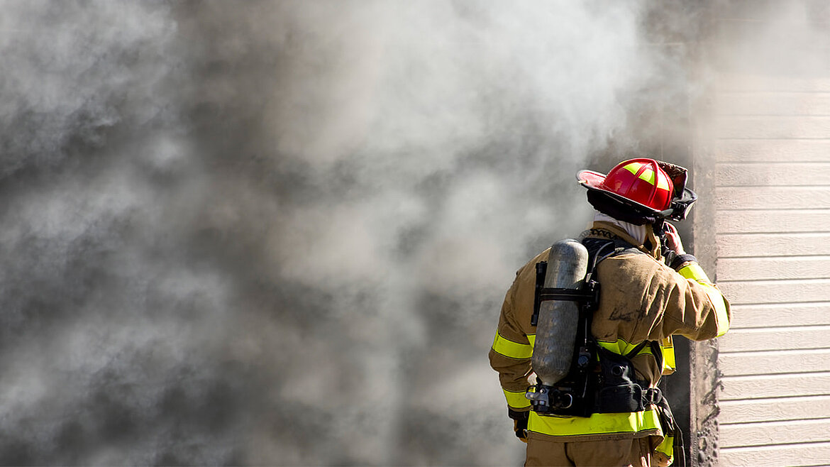 Feuerwehrmann vor brennendem Gebäude mit Brandrauch