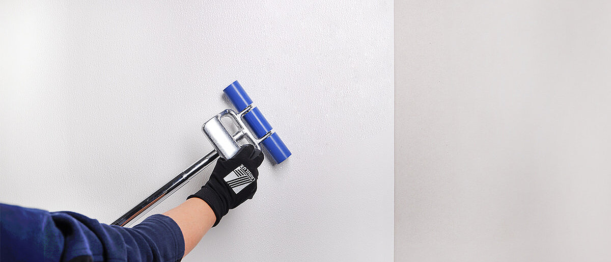 Person benutzt eine Walze, um eine weiße Platte an die Wand zu kleben
