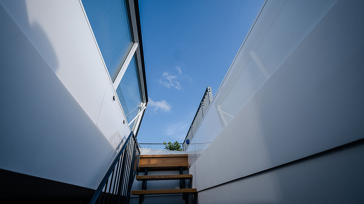 Treppe führt durch einen Flachdach Ausstieg auf die Dachterrasse mit blauem Himmel.