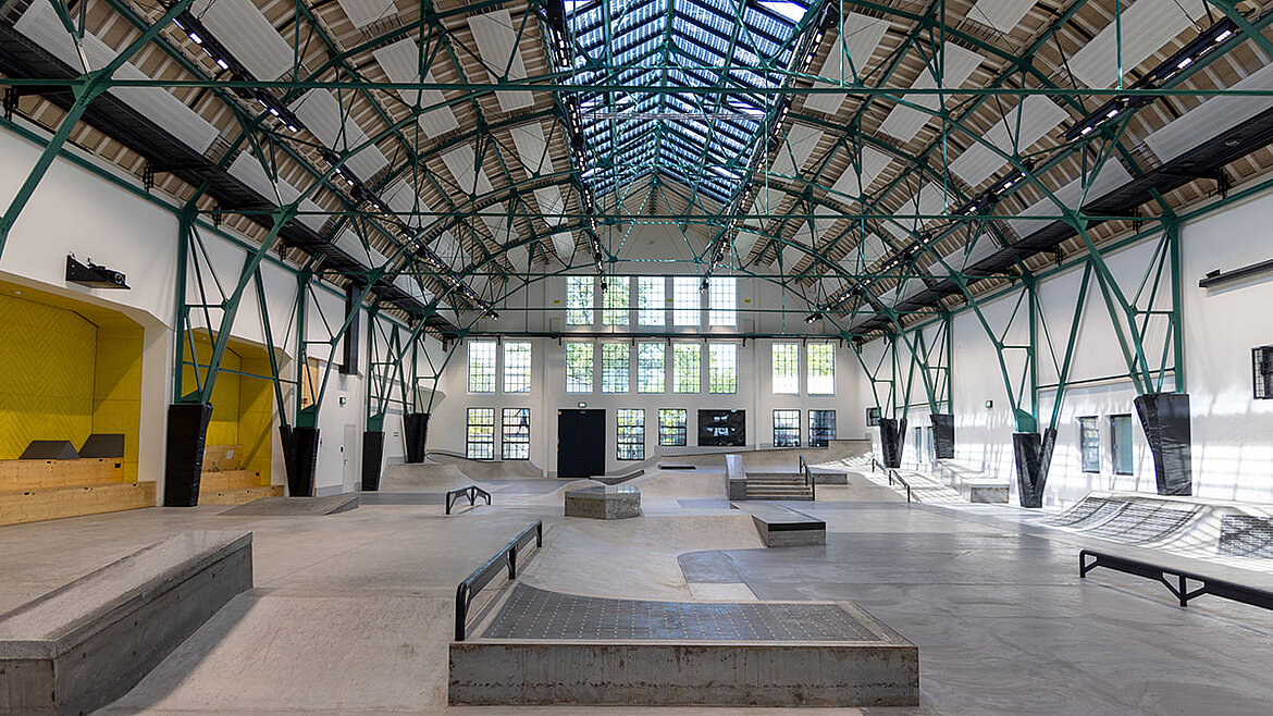Skaterhalle mit großflächigem Glasdach und Skatepark-Elementen im Innenraum