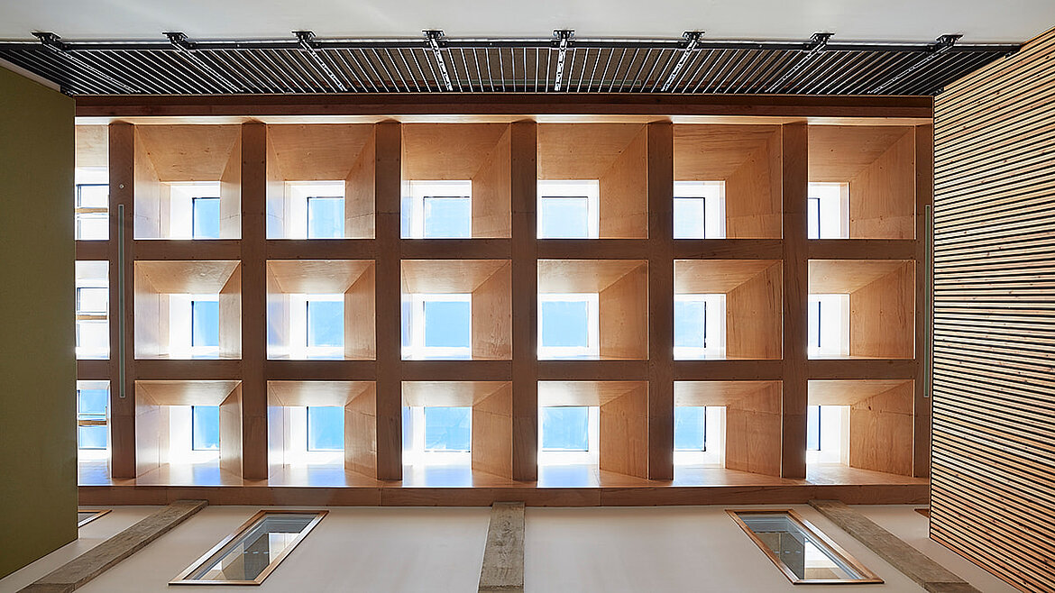 Innenansicht eines Atriums mit Holzlamellen und quadratischen Fensteröffnungen