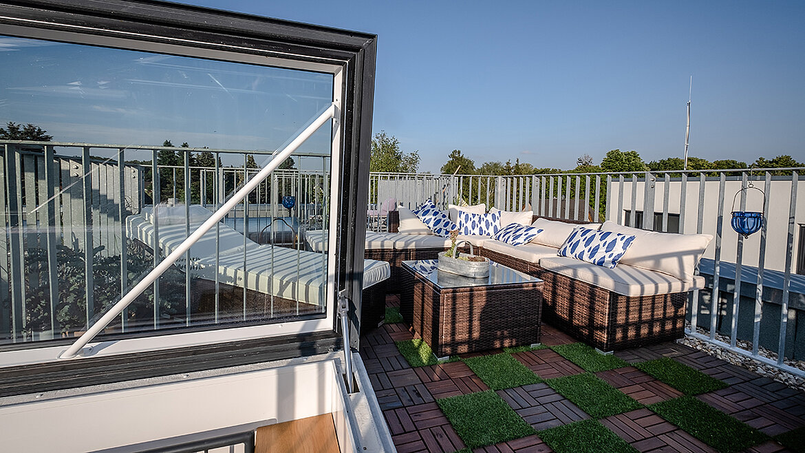 Moderne Dachterrasse mit Glasluke, Lounge-Möbeln und grüner Bodenverkleidung.