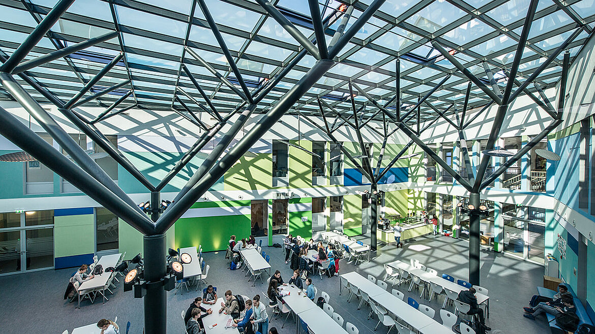 Stahlkonstruktion symbolisiert Bäume unter einem Glasdach Stahl-Glas-Konstruktion über der Schulaula der IS Bonn | insights by LAMILUX