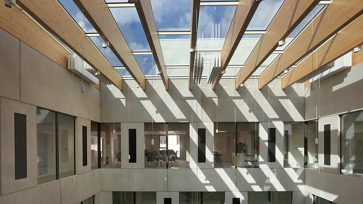 Modernes Atrium mit Glasdach und Holzstreben, das natürliches Licht hereinlässt.