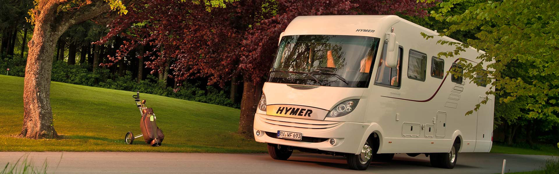 Wohnmobil fährt auf einer Straße durch einen grünen Park mit Bäumen