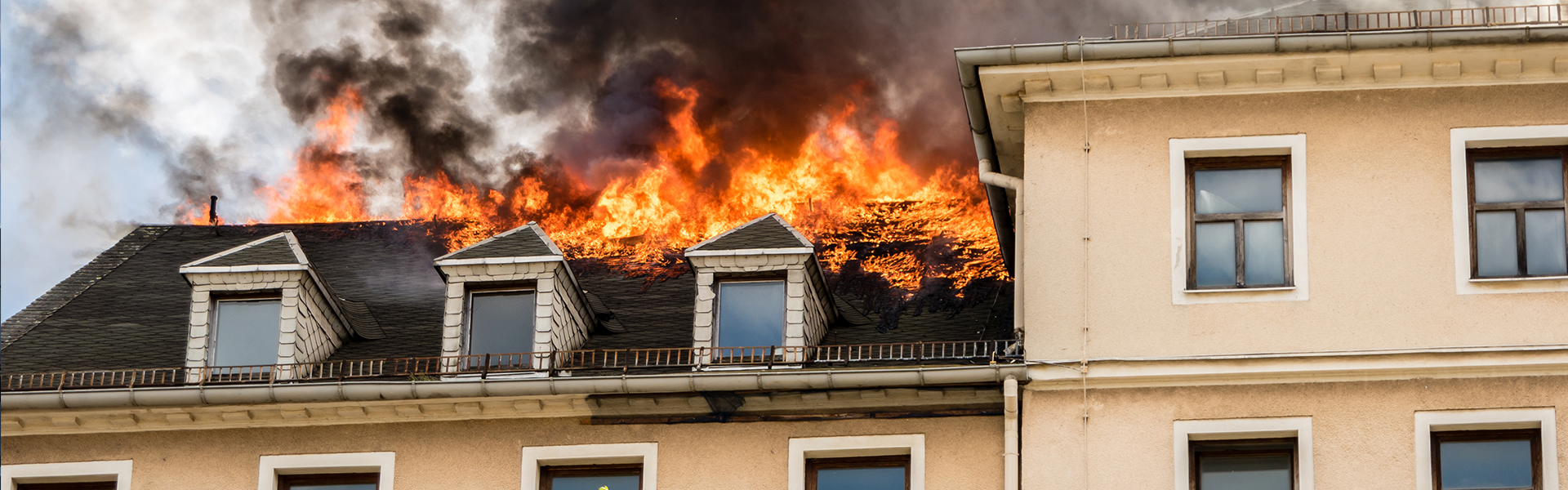Wohnhaus mit Dachbrand, Flammen und dichter schwarzer Rauch über dem Gebäude